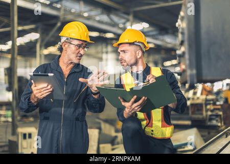 senior engineer talking explain machine working process for teaching training young male worker at heavy industry factory Stock Photo