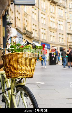 Close-up of a bicycle basket full of flowers on a street in Edinburgh's Old Town. Some unrecognizable passersby out of focus in the background. Vertic Stock Photo