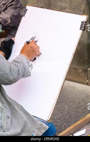 Unrecognizable street artist. Hand of a cartoonist holding a marker pen on a blank canvas. Vertical shot. Stock Photo