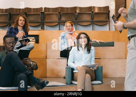 Concentrated diverse group of young businesspeople listening to a presentation and writing notes down in a notebook Stock Photo