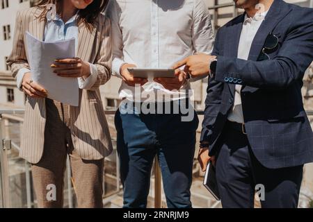 Three architects working together, male person pointing at blueprint on the lap top, discussing big project. Cropped photo Stock Photo
