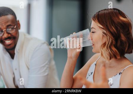 Lovely female employee drinking water during meeting while her black male colleague is explaining something to her. Stock Photo