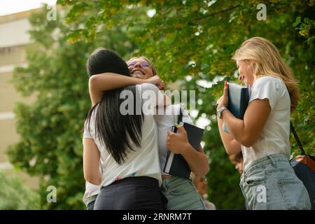 Two young university students greeting each other with a hug outside ready go back to school with backpacks and books in their hands Stock Photo
