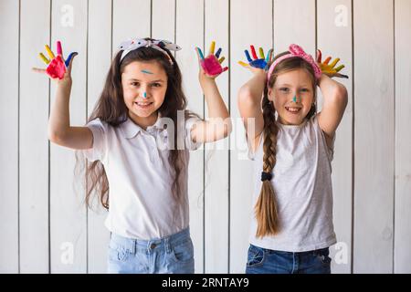 Smiling portrait two girls showing colorful painted hands standing against wooden wall Stock Photo