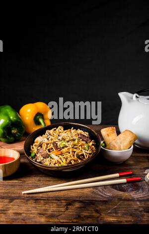 Chinese noodles with beef vegetables served with spring rolls wooden desk Stock Photo