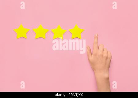 Female hand and four stars on pink background. Customer experience concept Stock Photo