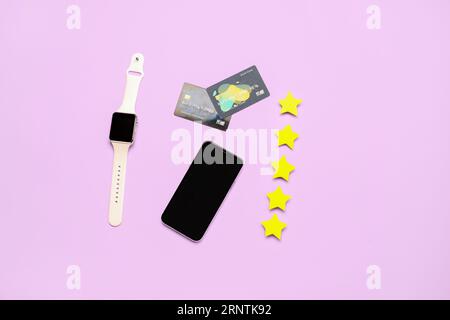 Five stars with mobile phone, smartwatch and credit cards on lilac background. Customer experience concept Stock Photo