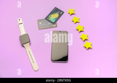 Five stars with mobile phone, smartwatch and credit cards on lilac background. Customer experience concept Stock Photo