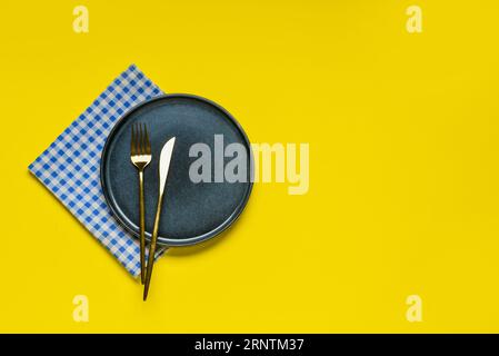 Empty plate with cutlery and blue checkered napkin on yellow background Stock Photo