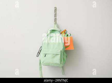 School backpack with different stationery hanging on light wall Stock Photo