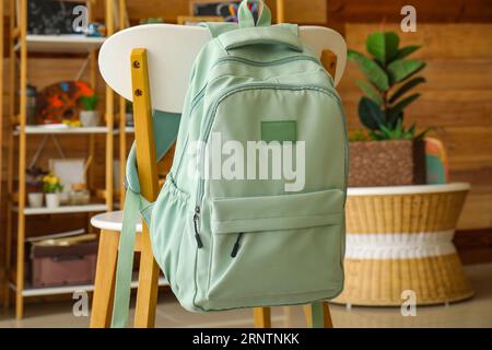 Stylish school backpack hanging on chair in room Stock Photo