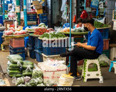 Two sellers of spicy chilies, in shades of red and green, sit by their stall in the open-air market of Bangkok, hoping for customers. Stock Photo