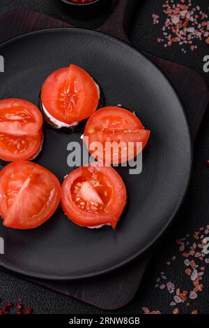 Delicious eggplant cut into circles grilled and cooked with mayonnaise and tomatoes on a dark concrete background Stock Photo