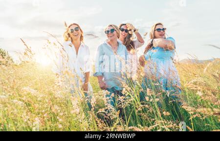 Portrait of four cheerful smiling and laughing women embracing during outdoor walking by high green grass hill. They looking at the camera. Woman frie Stock Photo