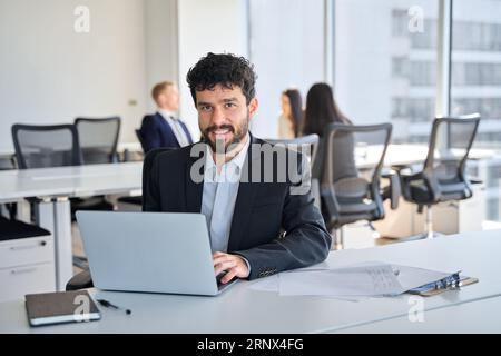 Smiling Latin young business man employee sitting at work with laptop. Stock Photo
