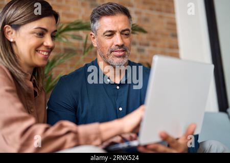 Smiling mature business man and woman having conversation looking at laptop. Stock Photo