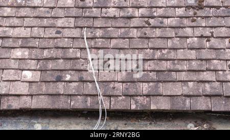 Cable exiting through a hole in an old tiled roof Stock Photo