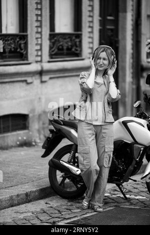 Woman with headphones standing on street near motorcycle. Black and white photo. Stock Photo
