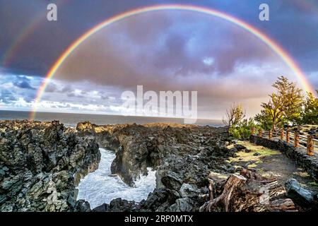 A vibrant rainbow arches over the cliffs of Saint-Leu on Réunion Island, captured from the coastline near the famous “Gouffre” during dramatic tropica Stock Photo