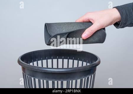 Male hand tosses a rolled worn and dirty mouse pad into a trash bin. Stock Photo