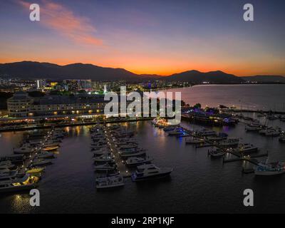 Night time sunset drone shot at Cairns Marina and Esplanade with orange sky and a mountain backdrop Stock Photo