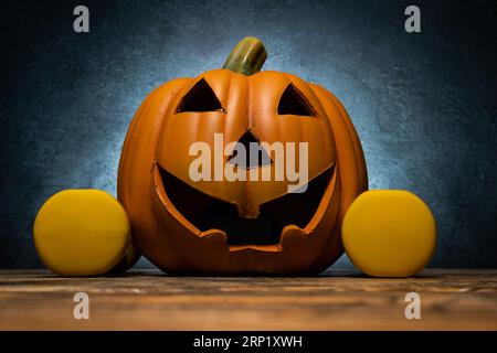 Spooky Halloween pumpkin decoration and dumbbells. Healthy fitness lifestyle autumn or fall composition. Gym workout and sport training concept. Stock Photo