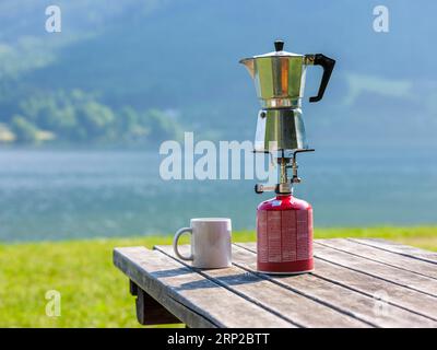 Espresso pot on a gas cooker next to a cup standing on a wooden table at the lake, Hallstaetter See, Upper Austria, Austria Stock Photo