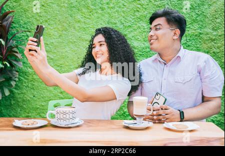 Two happy friends having a coffee and taking a selfie. Couple of friends sitting enjoying a coffee and taking a selfie Stock Photo