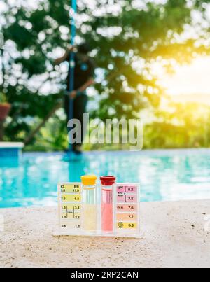 Water PH tester kit on the edge of the swimming pool with maintenance person in the background Stock Photo