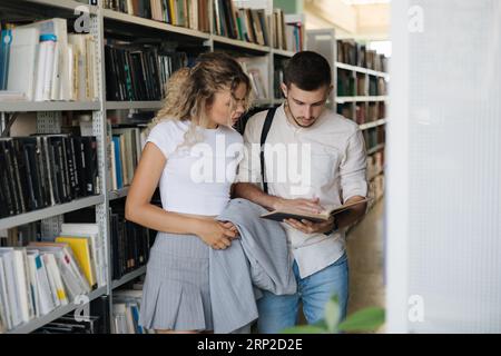 Handsome man and attractive female looking for book in university library. Woman show something to classmate in book Stock Photo