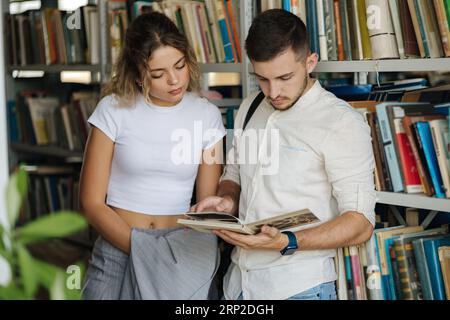 Handsome man and attractive female looking for book in university library. Woman show something to classmate in book Stock Photo