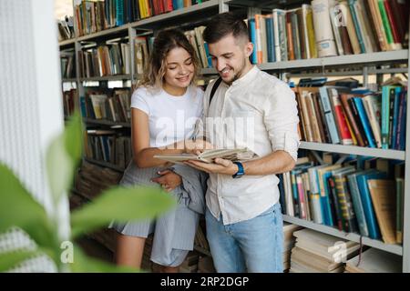 Handsome man and attractive female looking for book in university library. Woman show something to classmate in book Stock Photo