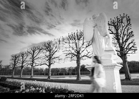 Ghost in the park. Black and white photography. A defocused person against the background of a moody sky and a sculpture of an angel. Dramatic poetic Stock Photo