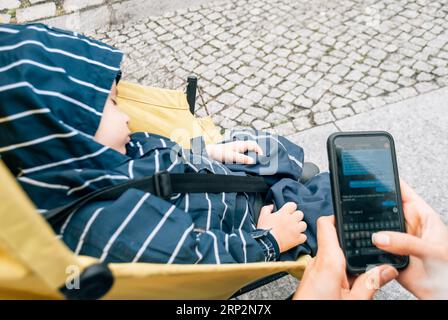 A woman corresponds via text messages in a messenger near a stroller with a small child Stock Photo