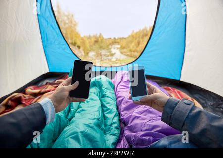 couple with phones in sleeping bags in camp tent Stock Photo