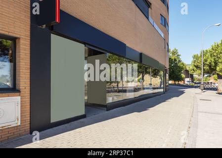 Image of a modern commercial premises at the foot of a wide street with plenty of trees with a large glass front on a very bright day Stock Photo