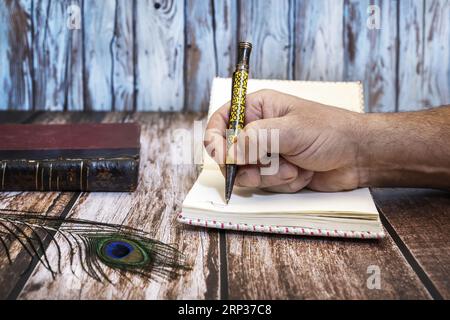 A man's hand writing in a small notebook with knitted covers with a vintage pen Stock Photo