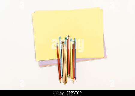 A few assorted colored graphite pencils with small erasers on one end on a few reams of A4 sized colored paper Stock Photo