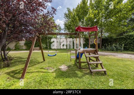 A wooden swing along with a slide on the grass of a garden in the common area of an urbanization Stock Photo