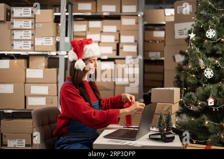 Female online store small business owner seller wrapping gift packing box preparing delivery parcel on table in warehouse. Ecommerce dropshipping sale Stock Photo