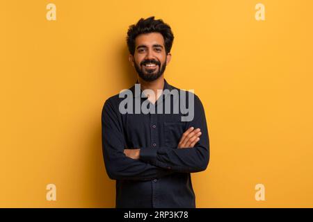Confident young indian man standing with folded arms over yellow background Stock Photo
