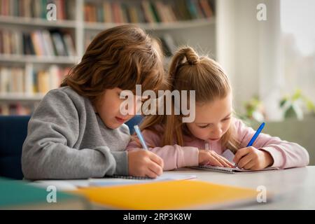 Attentive caucasian pupils boy and girl doing their homework or writing test, sitting at desk in classroom Stock Photo