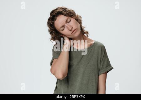 Tired sad young woman suffering from fatigued massaging hurt stiff neck rubbing tensed muscles to relieve joint pain. Symptom of cervical chondrosis. Inflammation of vertebra, fibromyalgia concept Stock Photo