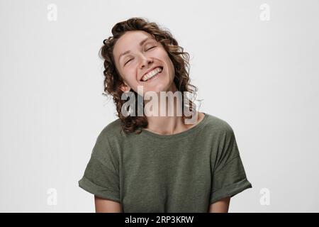 Emotional curly woman smiling widely, closing her eyes in expectation of surprise from her boyfriend, looking happy, feeling happiness, showing white teeth while having fun. Isolated on white Stock Photo