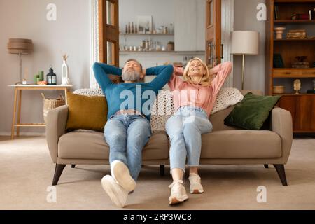 Senior Spouses Resting With Eyes Closed Leaning On Sofa Indoors Stock Photo