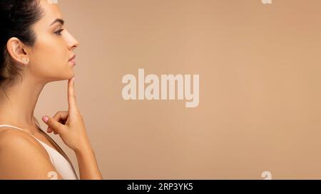Side view of millennial woman wearing top touching her chin Stock Photo