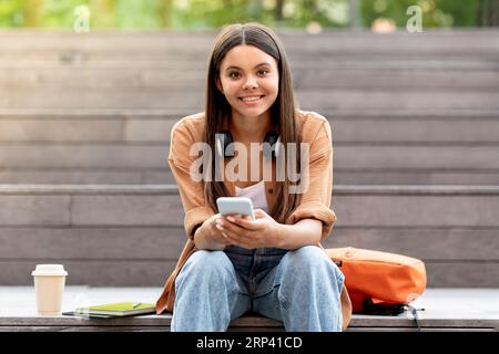 Portrait of cheerful young woman student using phone outtdoor Stock Photo