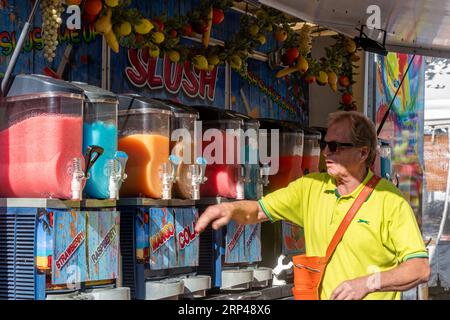 Slush stand with man selling colourful ice cold slushy fruit drinks at a market in Surrey, England, UK Stock Photo