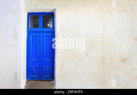 Blue wooden closed plank door on empty whitewashed stonewall background. Traditional Greek island architecture. Copy space Stock Photo