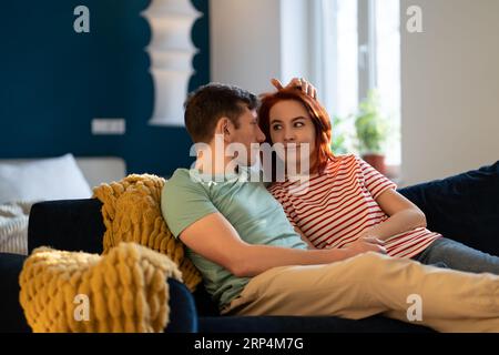 Caring man with loving woman sit on couch lovingly looking at each other hold hands romantic moment. Stock Photo